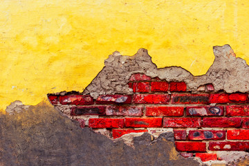 Distressed brick wall with cracks and broken yellow plaster half destroyed wall cover