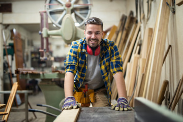 Portrait of young motivated carpenter standing by woodworking machine in his carpentry workshop.