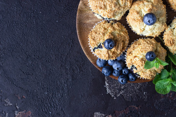 Blueberry muffins with fresh berries and mint leaves on dark brown stone background. Copy space.