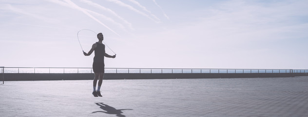 Muscular young man exercising with jumping rope on seafront