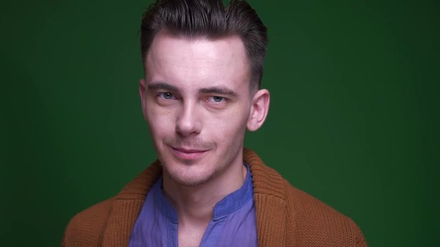 Closeup shoot of adult attractive man smiling with shynessl ooking at camera with background isolated on green