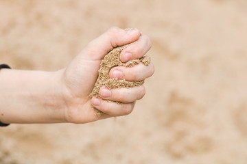 Child's hand close up squeezes the sand. Copy space.