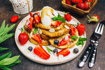 Stecked french toast topped with strawberries, blueberries, mint, ice cream and maple syrup