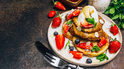 Stecked french toast topped with strawberries, blueberries, mint, ice cream and maple syrup