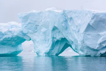 Fotobehang Beautiful turquoise blue iceberg floating in the Antarctic, against a foggy background © knelson20