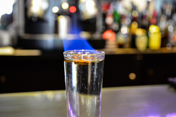 Vaso de shot con Licor de Sambuca flameada y granos de café en un bar.