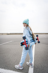 A girl in a hat and a blue sweater is holding a large longboard.