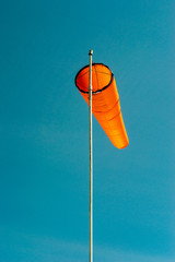 Downward angled plain orange windsock against a clear blue sky.