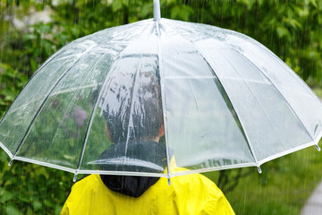 Boy in yellow raincoat holds transparent Umbrella during the rain. Rainy weather at spring, summer