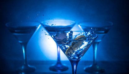 Martini cocktail glass in hand splashing on dark toned smoky background or colorful cocktail in glass with splashes and olives. Party club entertainment. Mixed light. Selective focus