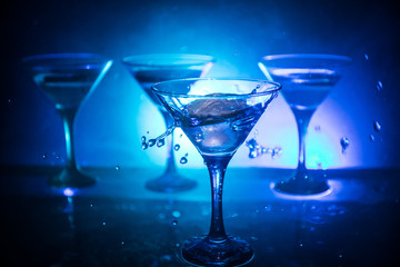 Martini cocktail glass in hand splashing on dark toned smoky background or colorful cocktail in glass with splashes and olives. Party club entertainment. Mixed light. Selective focus