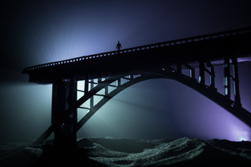 Artwork decoration. Silhouette of powerful metallic bridge at night with foggy backlight. Silhouette of person standing on bridge.