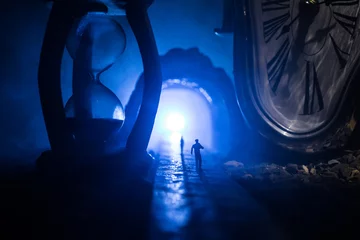 Zeitkonzept. Silhouette eines Mannes, der zwischen Sanduhren mit Rauch und Lichtern auf dunklem Hintergrund steht. Surreal dekoriertes Bild © zef art