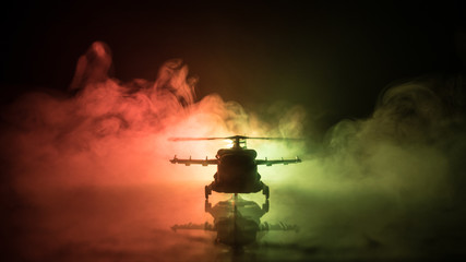Naklejka premium Silhouette of military helicopter ready to fly from conflict zone. Decorated night footage with helicopter starting in desert with foggy toned backlit. Selective focus.