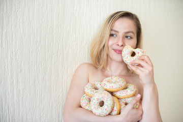Nude young woman eating donuts. Portrait of an attractive woman with a mountain of donuts