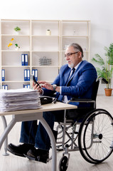 Aged employee in wheelchair working in the office 