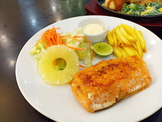 one piece of baked salmon grilled pepper lemon and salt on a white plate with lettuce leaves and pileapple