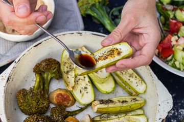Baked, roasted vegetables on frying pan skillet. Potato, zucchini, potato with spices. Woman hands adds soy sauce.