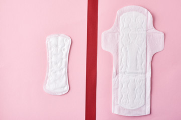 Two sanitary pads and red ribbon on a pink background