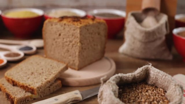 Healthy fresh multicereal and multigrain bread, with the various ingredients around - tabletop mill making whole grain flour, camera push in and refocus on various elements