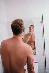 Attractive muscular man preparing himself in front of mirror in the bathroom