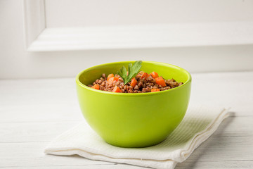 Green bowl of tasty buckwheat porridge on white wooden table.