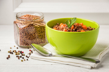 Green bowl of tasty buckwheat porridge on white wooden table.