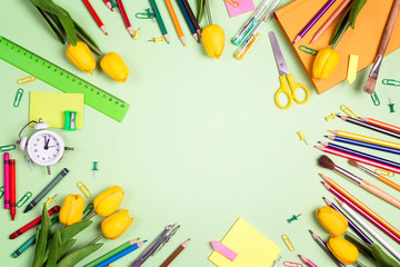 Flat lay frame composition from school supplies and yellow tulips on a green background. The concept of the teacher's day.