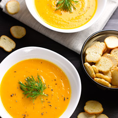 Pumpkin cream soup with croutons and fresh dill and parsley on dark wooden background, top view