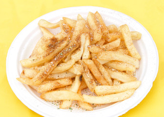 White paper plate with seasoned french fries on yellow table cloth. Popular street fair food.