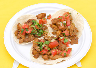 White paper plate with chicken street tacos on yellow table cloth. Popular street fair food.