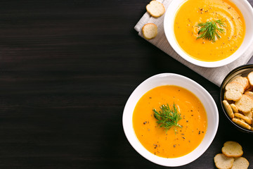 Pumpkin cream soup with croutons and fresh dill and parsley on dark wooden background, top view