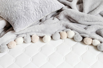 Grey blanket with pompoms on the new mattress.