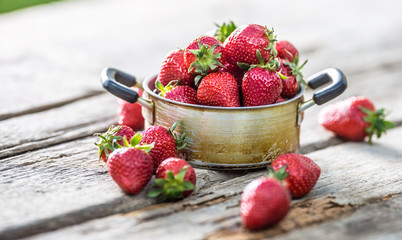Fresh ripe strawberries in vintage kitchen pot on old garden table