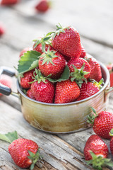 Fresh ripe strawberries in vintage kitchen pot on old garden table