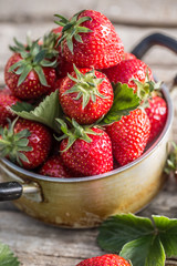 Fresh ripe strawberries in vintage kitchen pot on old garden table
