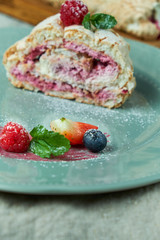Meringue cake roll slice on a plate with berries, on a gray background