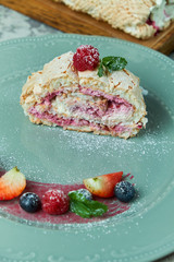 Meringue cake roll slice on a plate with berries, on a gray background