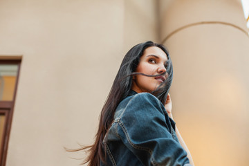 young brunette girl in a gray shirt and jeans jackett walking around city in the wind. Concept of...
