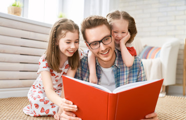 father reading a book to his daughters