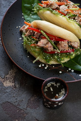 Dark plate with steamed chinese bao on a brown stone surface, vertical shot, elevated view