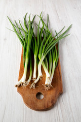 Fresh green onions on a rustic wooden board over white wooden background, side view.