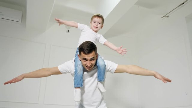 Dad plays with son sitted on his shoulders, they spread their arms out to the sides depicting a plane.