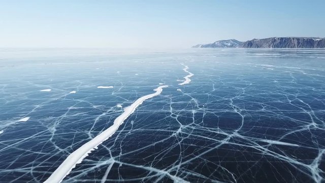 Drone rises above the frozen crystal ice of the lake Baikal. Top view. Natural background and patterns