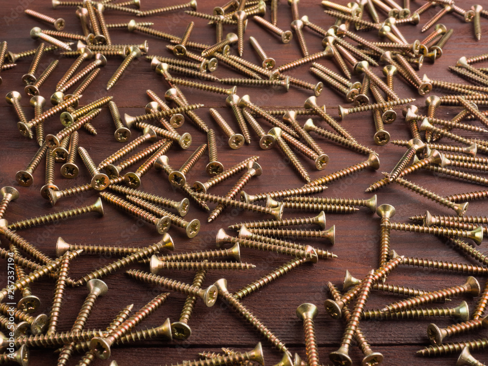 Wall mural set of metal screws on a brown wooden background. industrial background