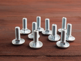 Group of silver color steel screws on brown background