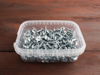 Fototapeta premium Group of silver color steel screws in box, on brown background. Industrial theme