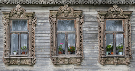 Obraz premium Three village windows with carved platbands and a cornice of the national Russian style against the background of aged faded wooden boards
