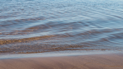 Shallow transparent water background with waves washing over pink beach sand