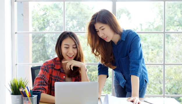  Two young asian women working with laptop computer at home office with happy emotion moment, working at home, small business, office casual lifestyle concept